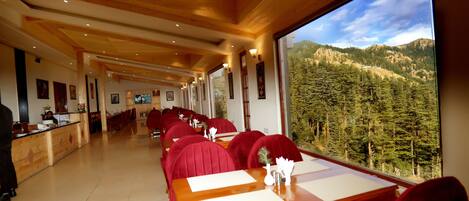 Un ristorante con interni in legno, sedie imbottite rosse e vista su una montagna boscosa.