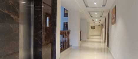 A modern hotel corridor with marble walls, a wooden railing, and a clean, tiled floor.
