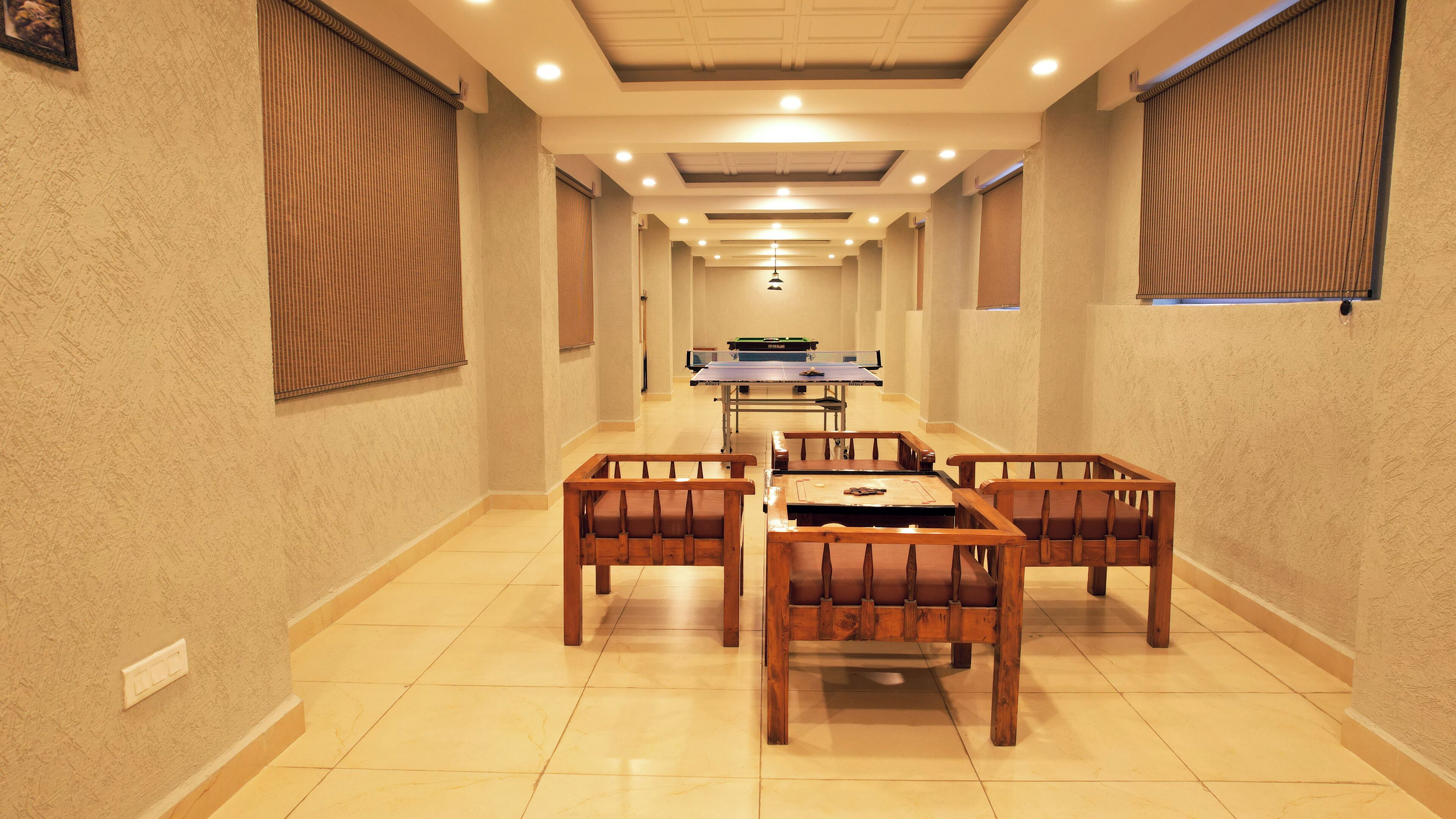 A hotel lobby with a ping pong table, wooden chairs, and a tiled floor.