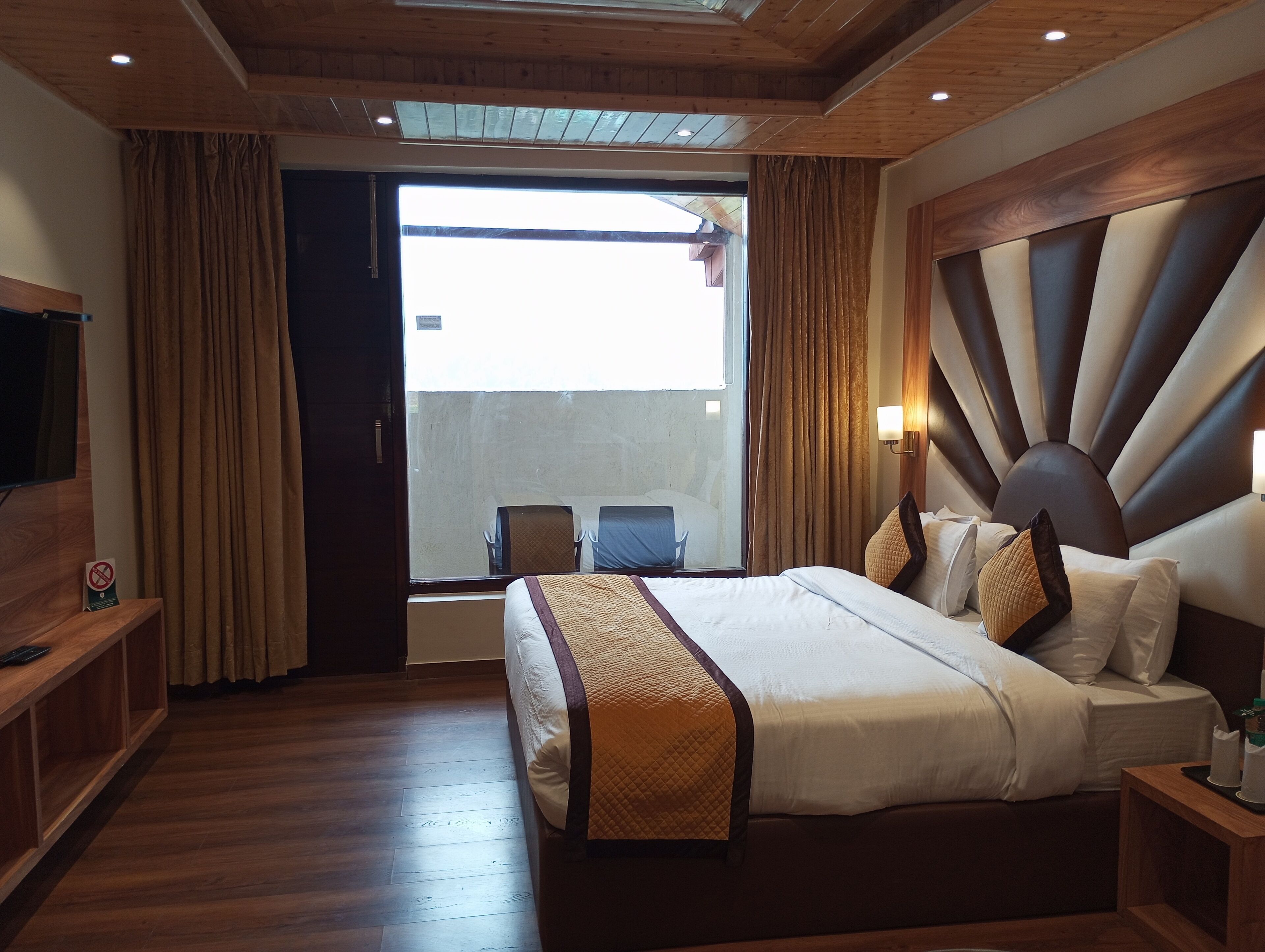 Habitación de hotel con una cama grande, piso de madera, un televisor sobre un mueble de madera y vistas a través de un ventanal.