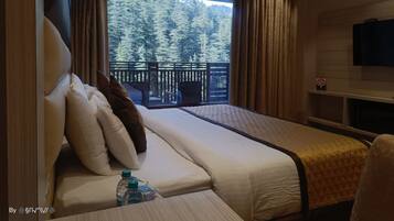 A hotel room with a bed, a TV, a window with a view of trees, and a balcony.