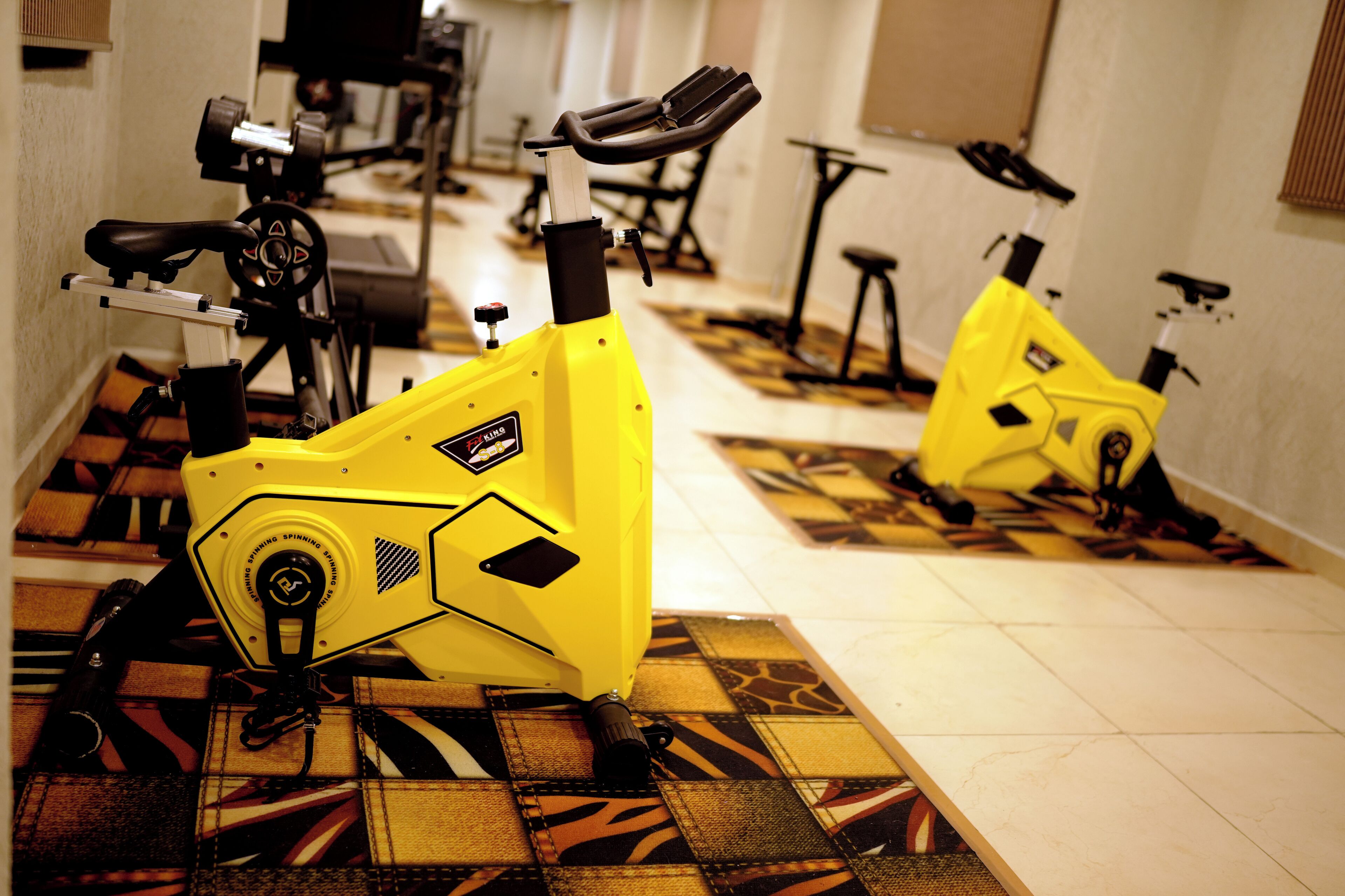 Two stationary bikes in a room with patterned flooring and a tiled wall.