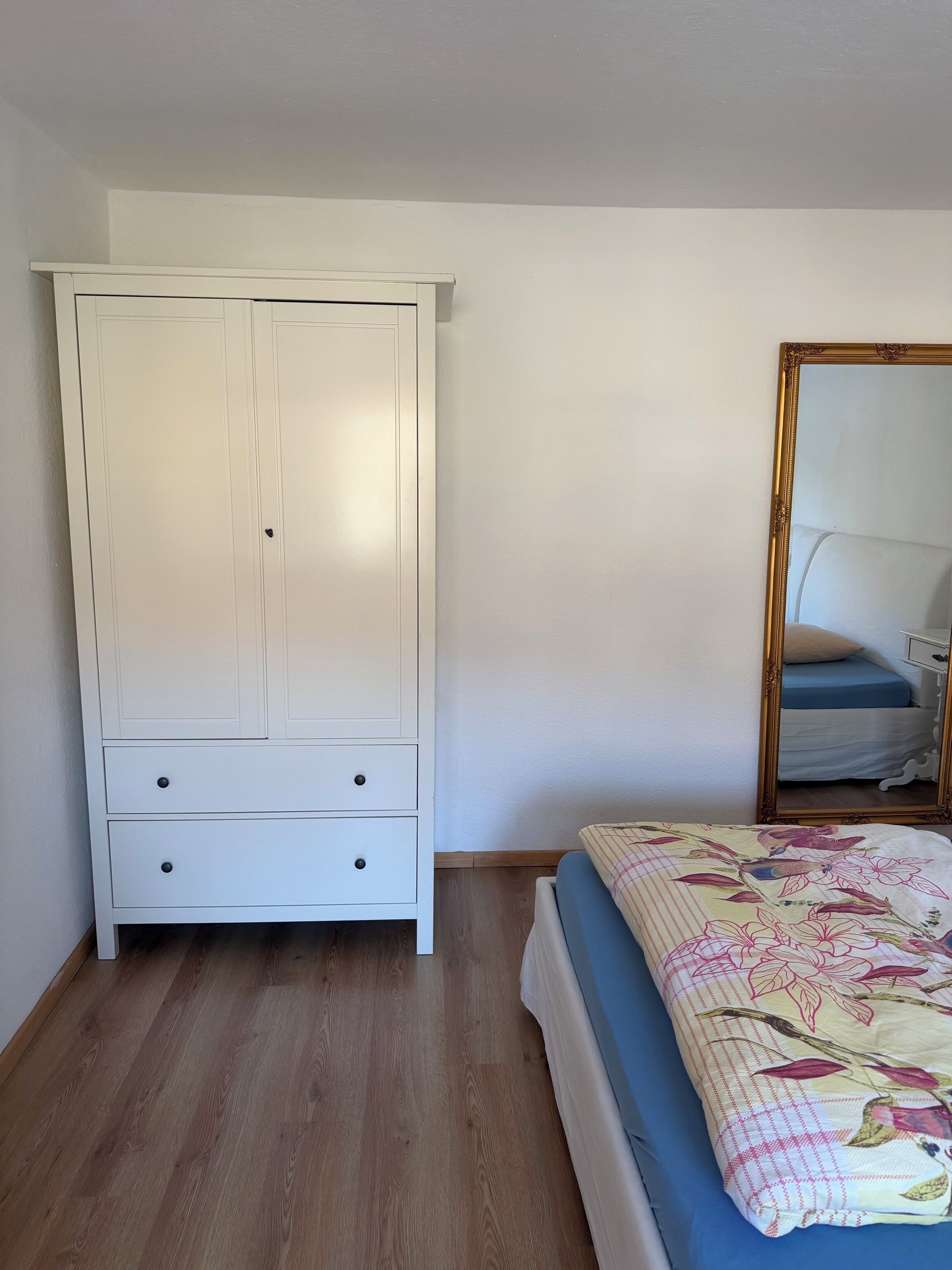 Een slaapkamer met een bed, een witte kledingkast en een spiegel.