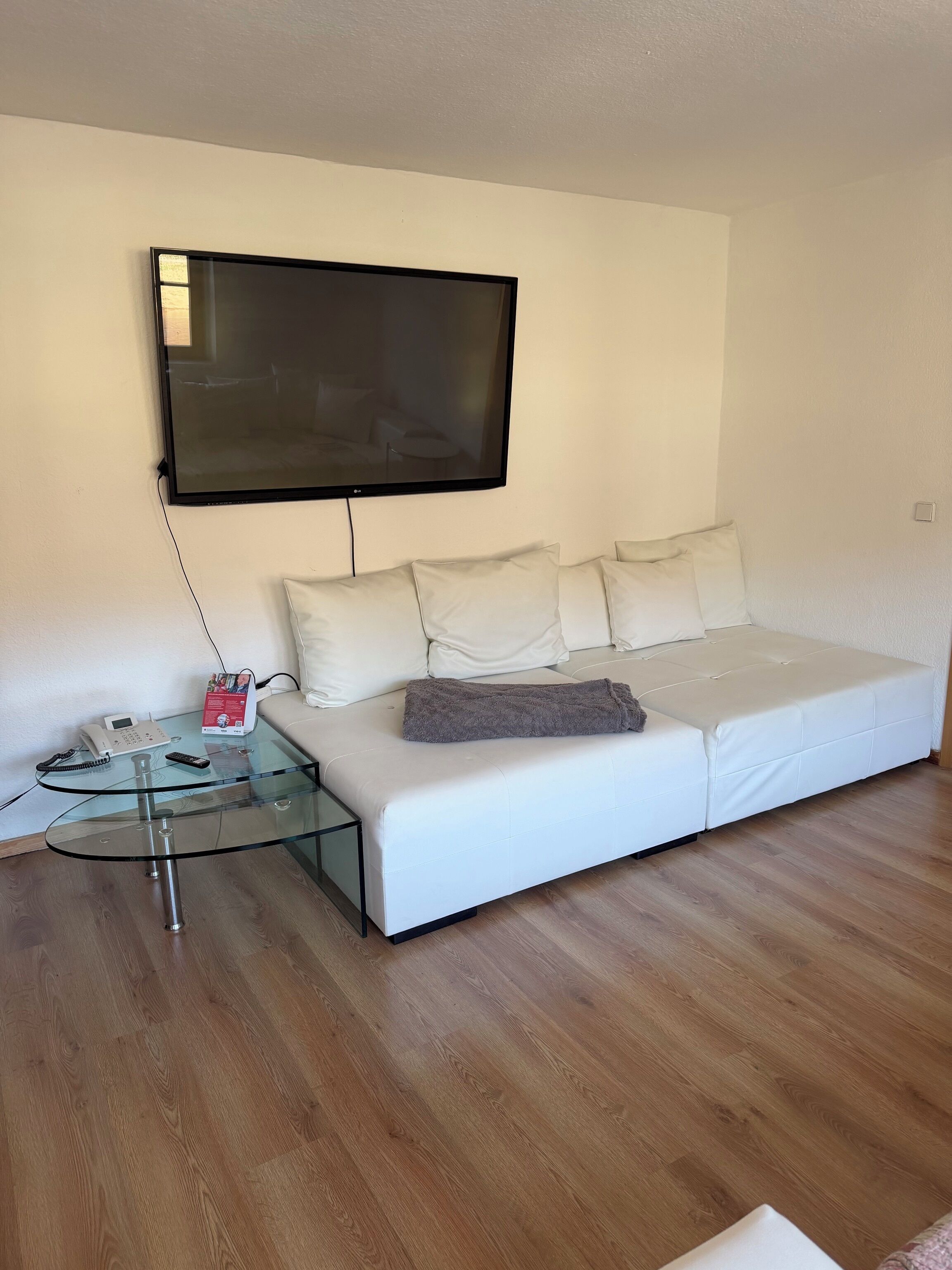Un soggiorno moderno con un divano bianco, un tavolino in vetro, una TV a parete e un telefono su un altro tavolino in vetro.