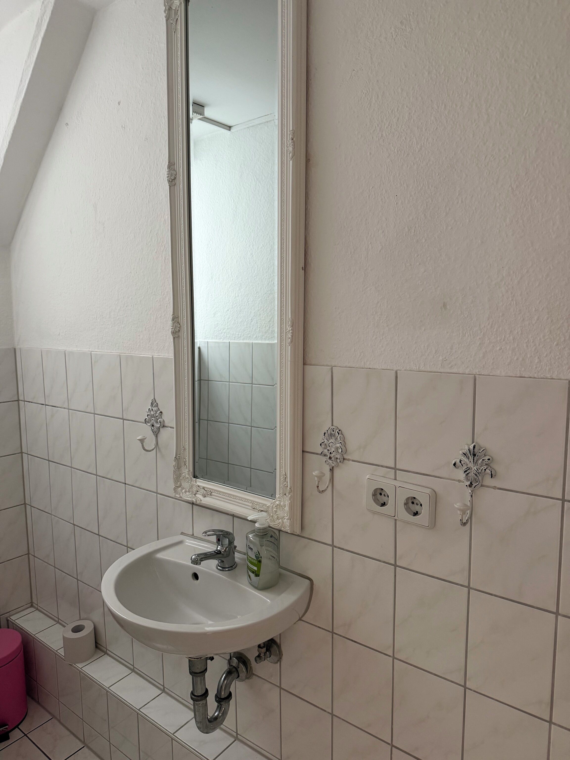 A bathroom with a white sink, mirror, and tiled walls.