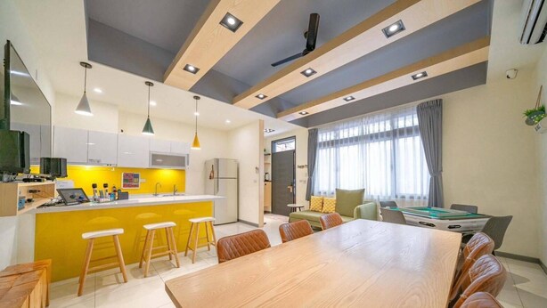 A modern kitchen with a yellow island, wooden stools, and a dining area with a wooden table and leather chairs. - New Forest Living Homestay (Wujie)