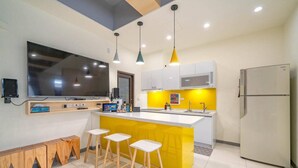 A modern kitchen with a central island, bar stools, a large flat-screen TV, pendant lights, and a refrigerator. - New Forest Living Homestay (Wujie)