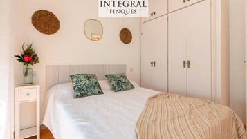 Een slaapkamer met een bed, twee kussens, een nachtkastje met een vaas en een kledingkast.