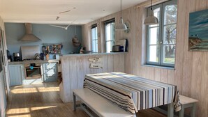 Una cocina con armarios de madera, una estufa y una cesta colgante. Hay un banco y una mesa con mantel a rayas.