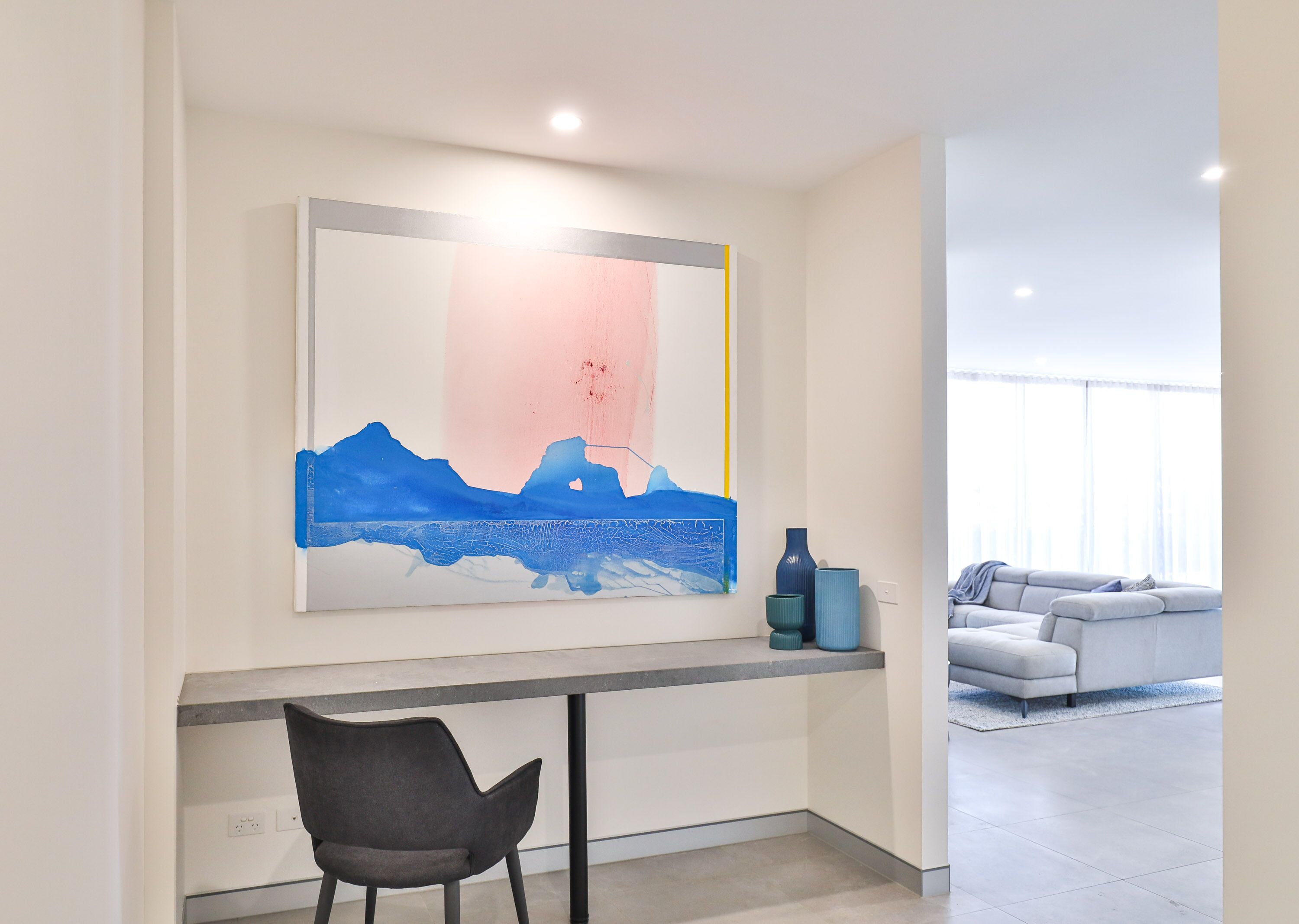 Una sala de estar moderna con un cuadro grande, un sofá gris y una pequeña mesa con una silla.