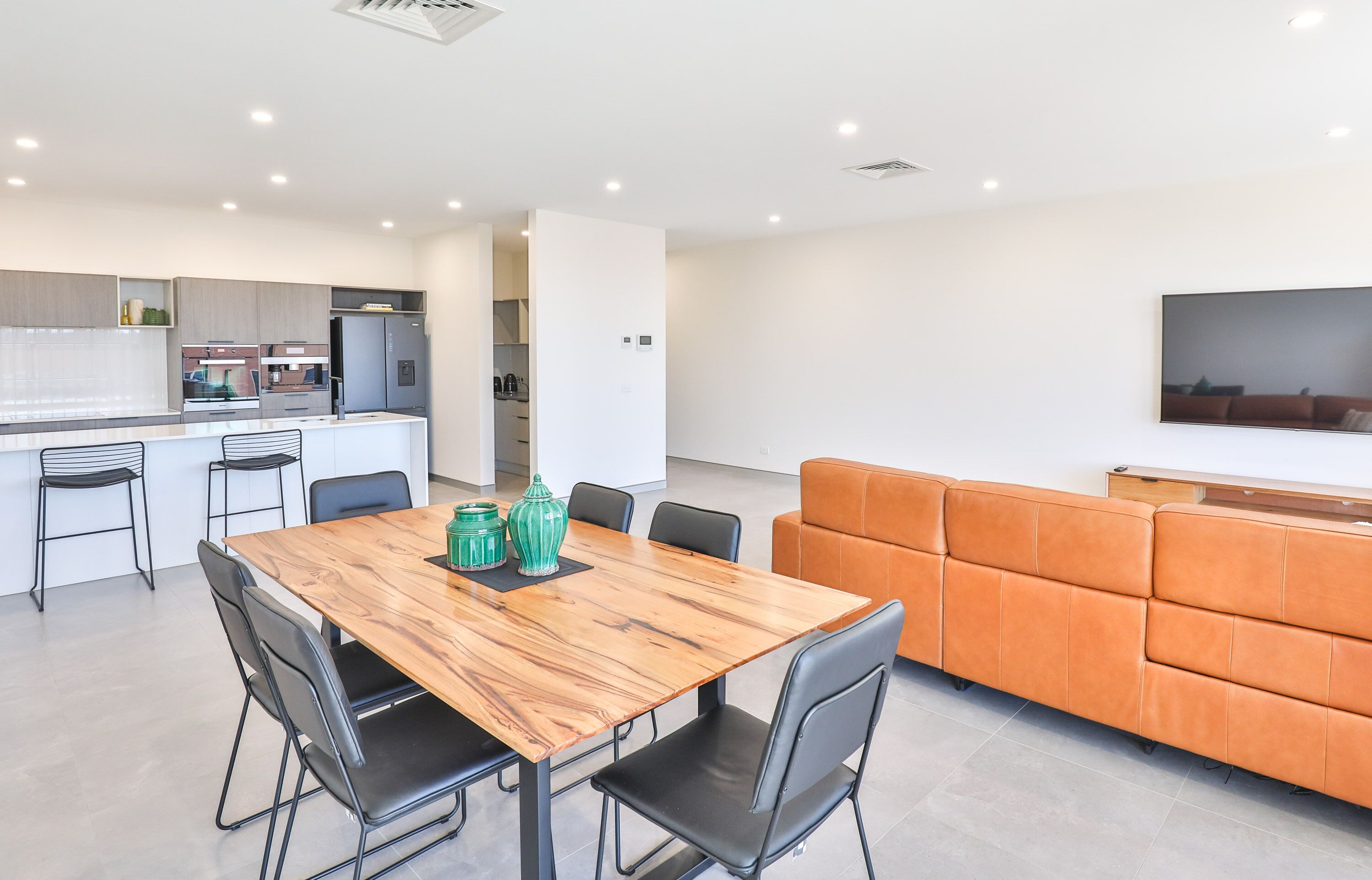 A modern kitchen with a dining area, a sofa, and a flat-screen TV.