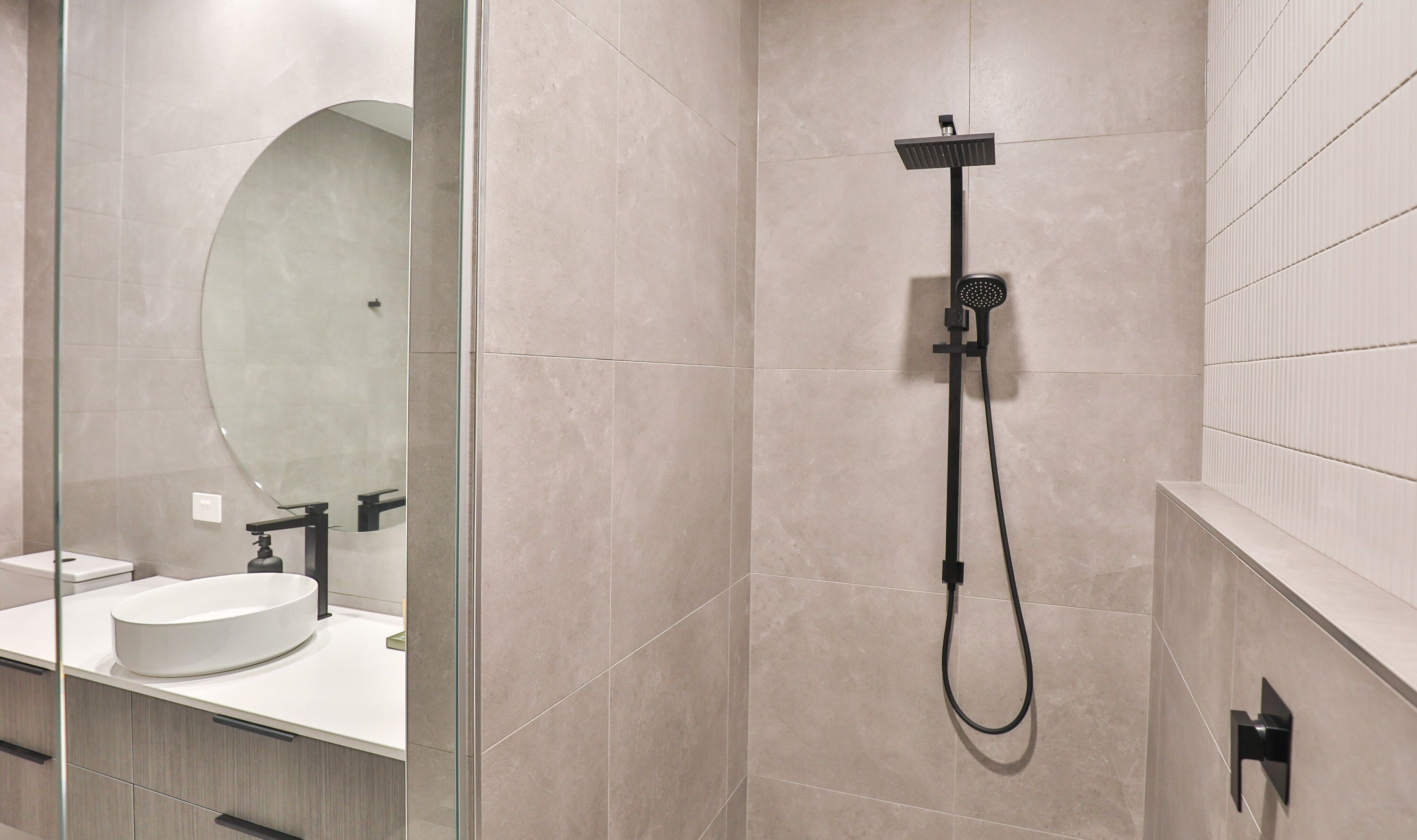A modern bathroom with a glass shower enclosure, a large mirror, and a white sink.
