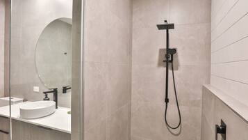 A modern bathroom with a glass shower enclosure, a large mirror, and a white sink.