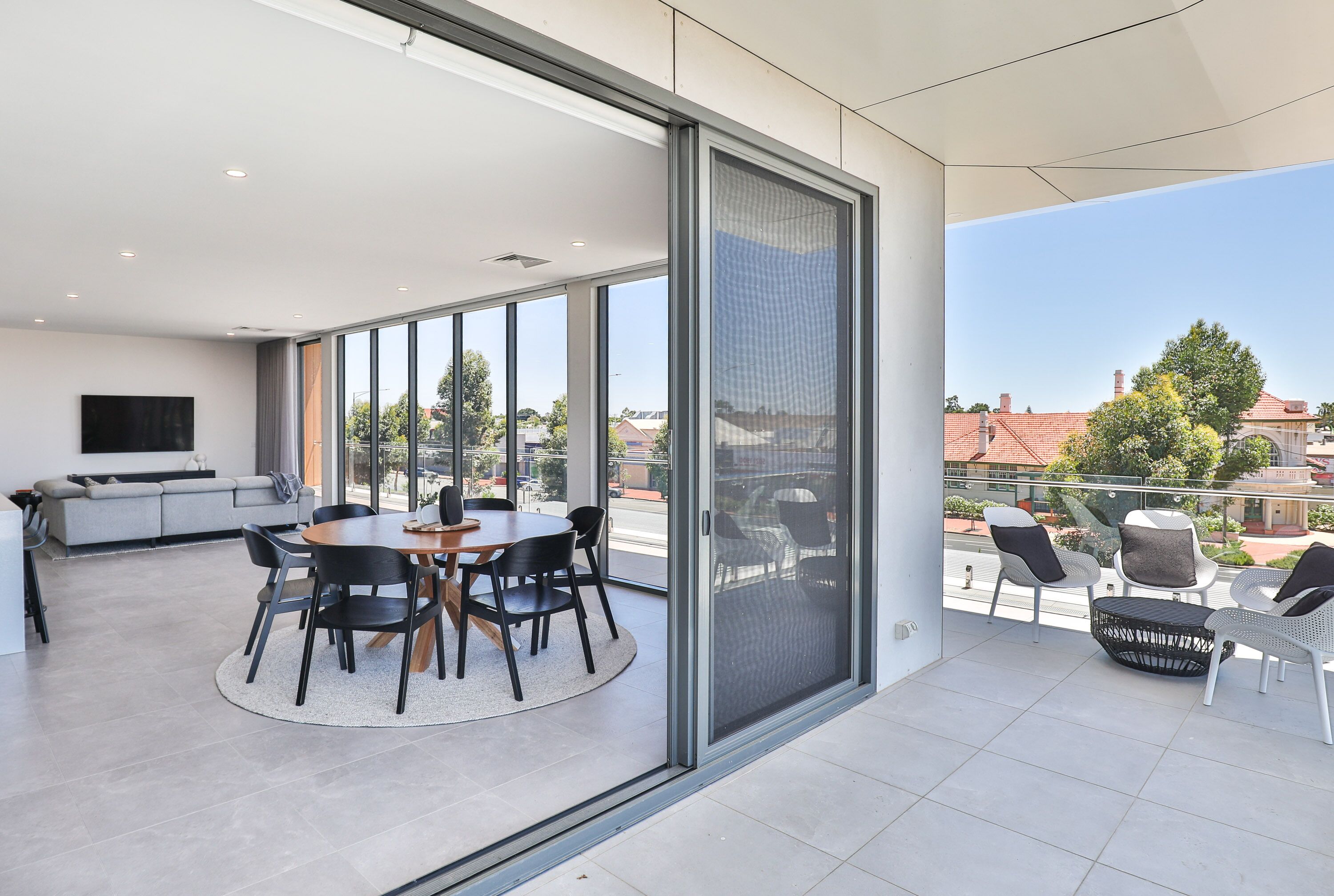 Un espacio habitable moderno con comedor, sofá y balcón con mobiliario exterior.