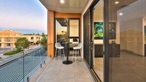 A balcony with a glass door, two white chairs, and a small table. - Indulge Apartments City View Penthouses (Mildura)