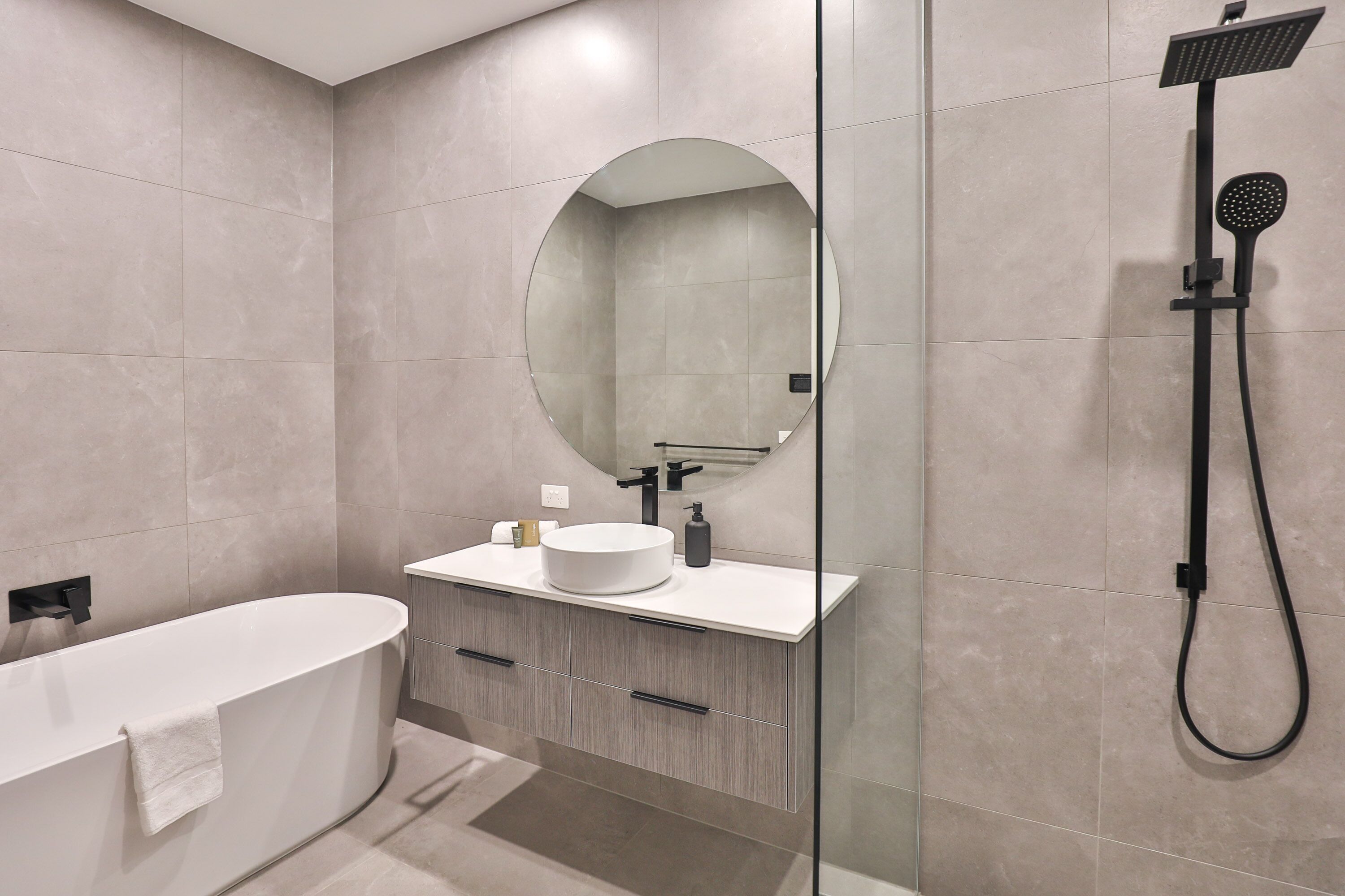 Un baño moderno con una bañera independiente, un espejo redondo y un cabezal de ducha empotrado.