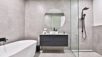 A modern bathroom with a freestanding bathtub, a round mirror, a glass-enclosed shower, and a dark-toned vanity.