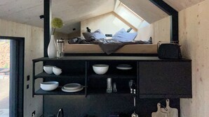 Quarto compacto com cama beliche, claraboia e prateleira preta com tigelas e pratos.
