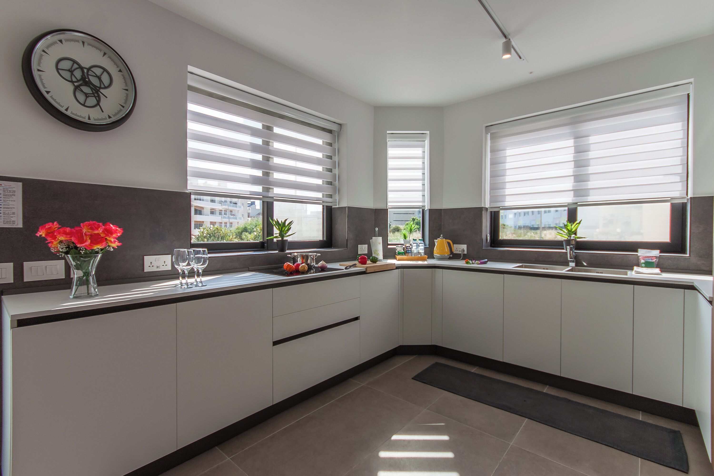 Una cocina moderna con armarios blancos, una encimera negra y un reloj en la pared.