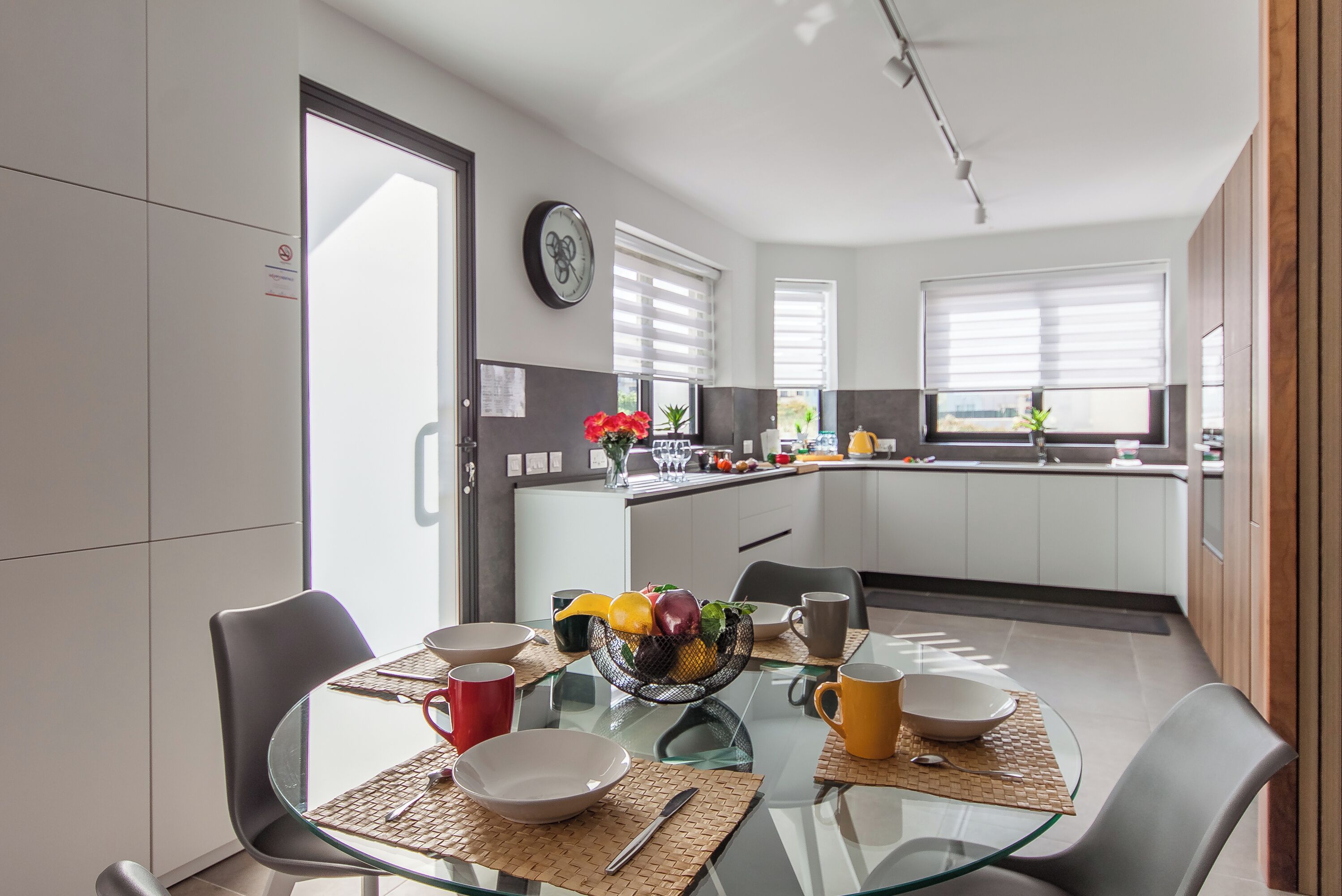 Una cocina moderna con armarios blancos, una mesa de comedor de vidrio y un frutero.