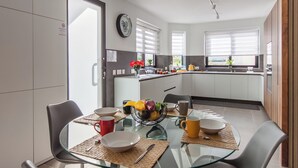 Una cucina moderna con mobili bianchi, un tavolo da pranzo in vetro e una ciotola di frutta.