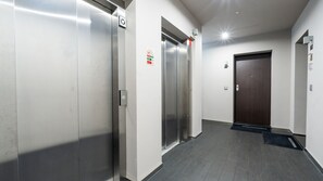A hallway with two elevators, a wooden door, and a fire safety sign.