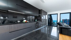 Eine moderne Küche mit dunklen Schränken, einem Edelstahl-Kochfeldabzug und Blick auf das Meer durch große Glasüren.