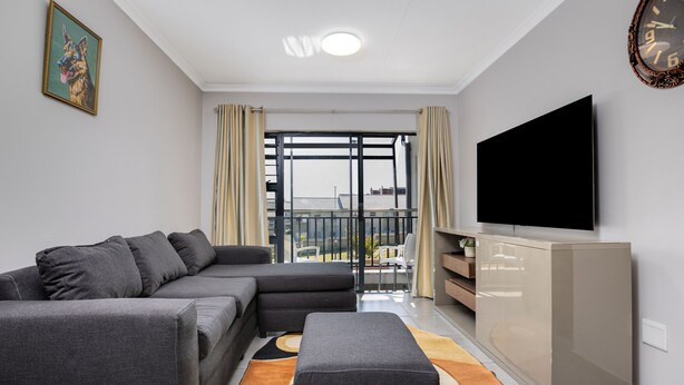 Una sala moderna con un sofá modular gris, un televisor de pantalla plana y un balcón con cortinas.