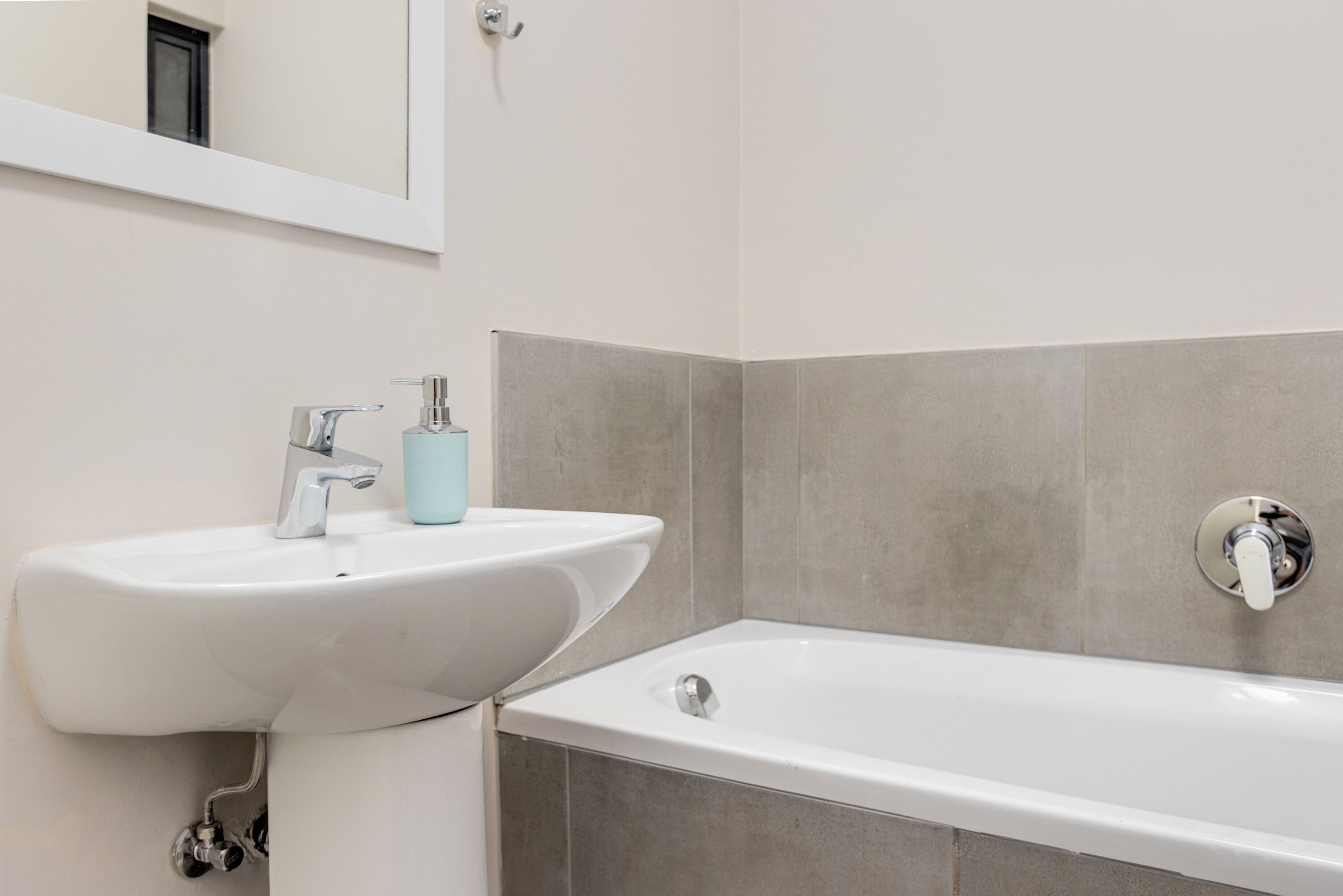 Une salle de bain avec un lavabo blanc, un distributeur de savon bleu et une baignoire blanche.