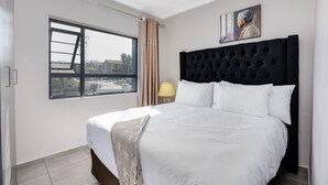 Habitación de hotel con una cama grande, una ventana con cortinas, una lámpara y un cuadro en la pared.
