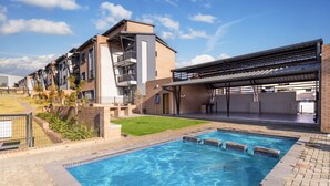 Un moderno edificio de apartamentos con piscina, mobiliario exterior y un patio cubierto.