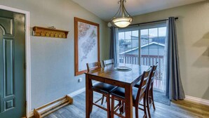 A dining area with a wooden table, chairs, a hanging light fixture, a map on the wall, and a view through a large window. - Adorable Alcove 2 Bedroom Escape Sleeps 4 (Kodiak)