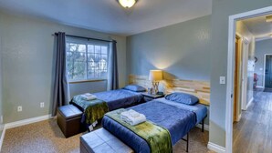 A room with two beds, a window with curtains, a lamp, and a door leading to another room. - Adorable Alcove 2 Bedroom Escape Sleeps 4 (Kodiak)
