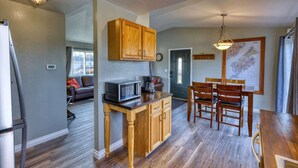 A kitchen with wooden cabinets, a microwave, and a dining area with chairs and a table. - Adorable Alcove 2 Bedroom Escape Sleeps 4 (Kodiak)
