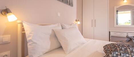 A neatly made bed with white bedding and pillows, a bedside lamp, a wall-mounted artwork, and a wardrobe with a mirror.