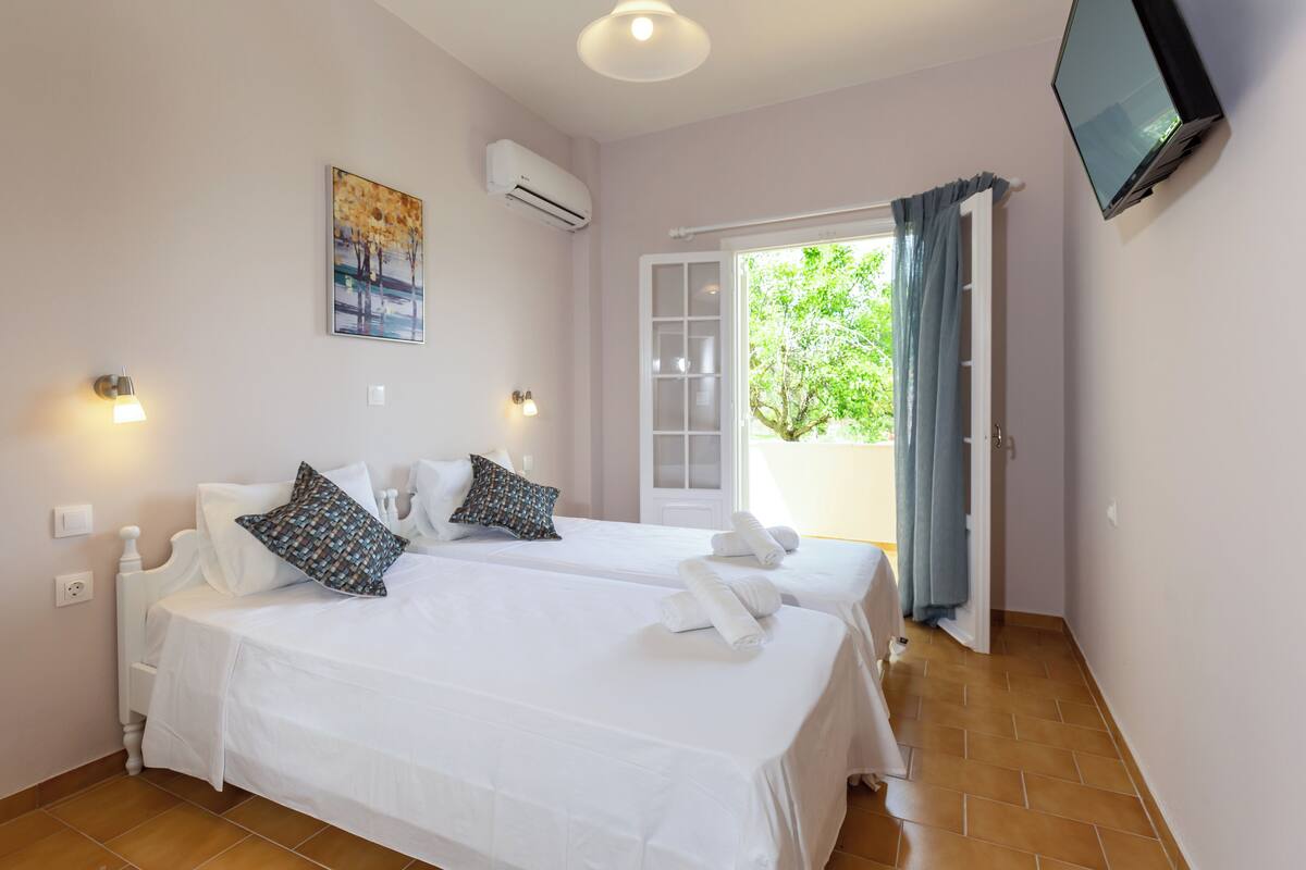 A hotel room with two beds, a TV, an air conditioner, and a window with curtains.