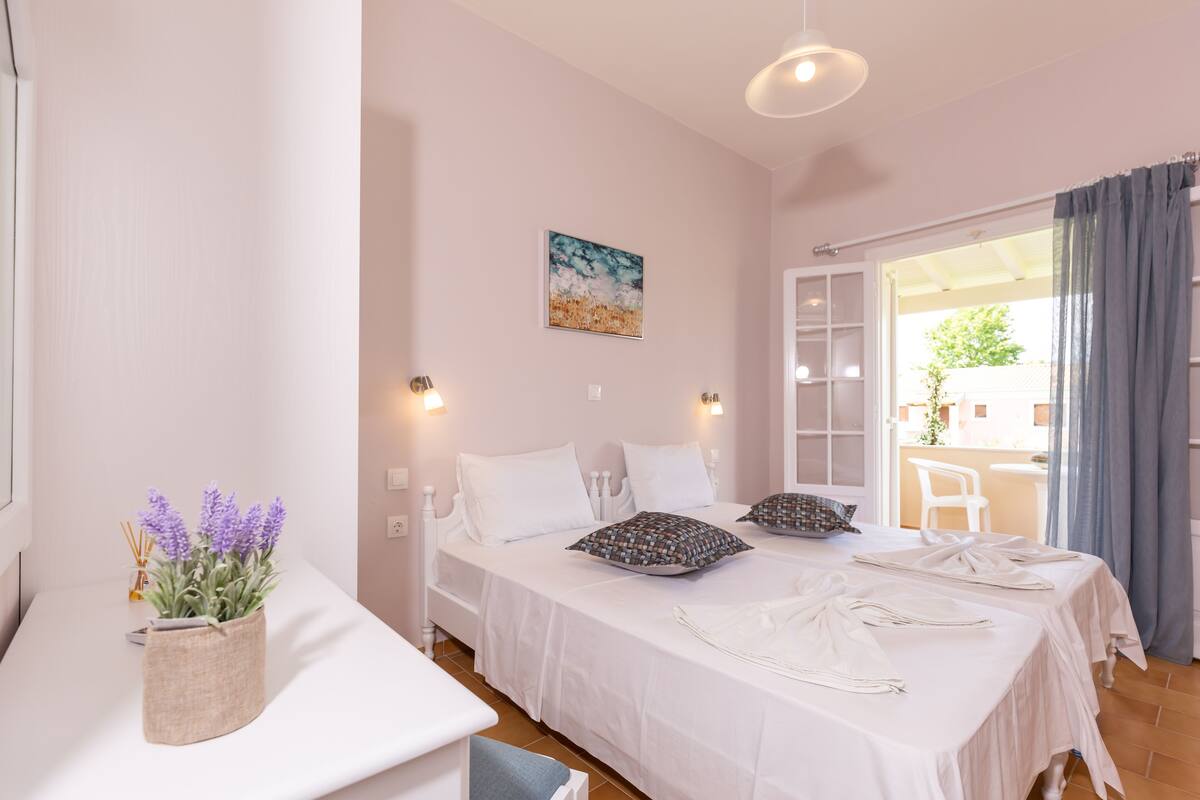A bedroom with two beds, a window with curtains, a painting on the wall, and a plant on the bedside table.