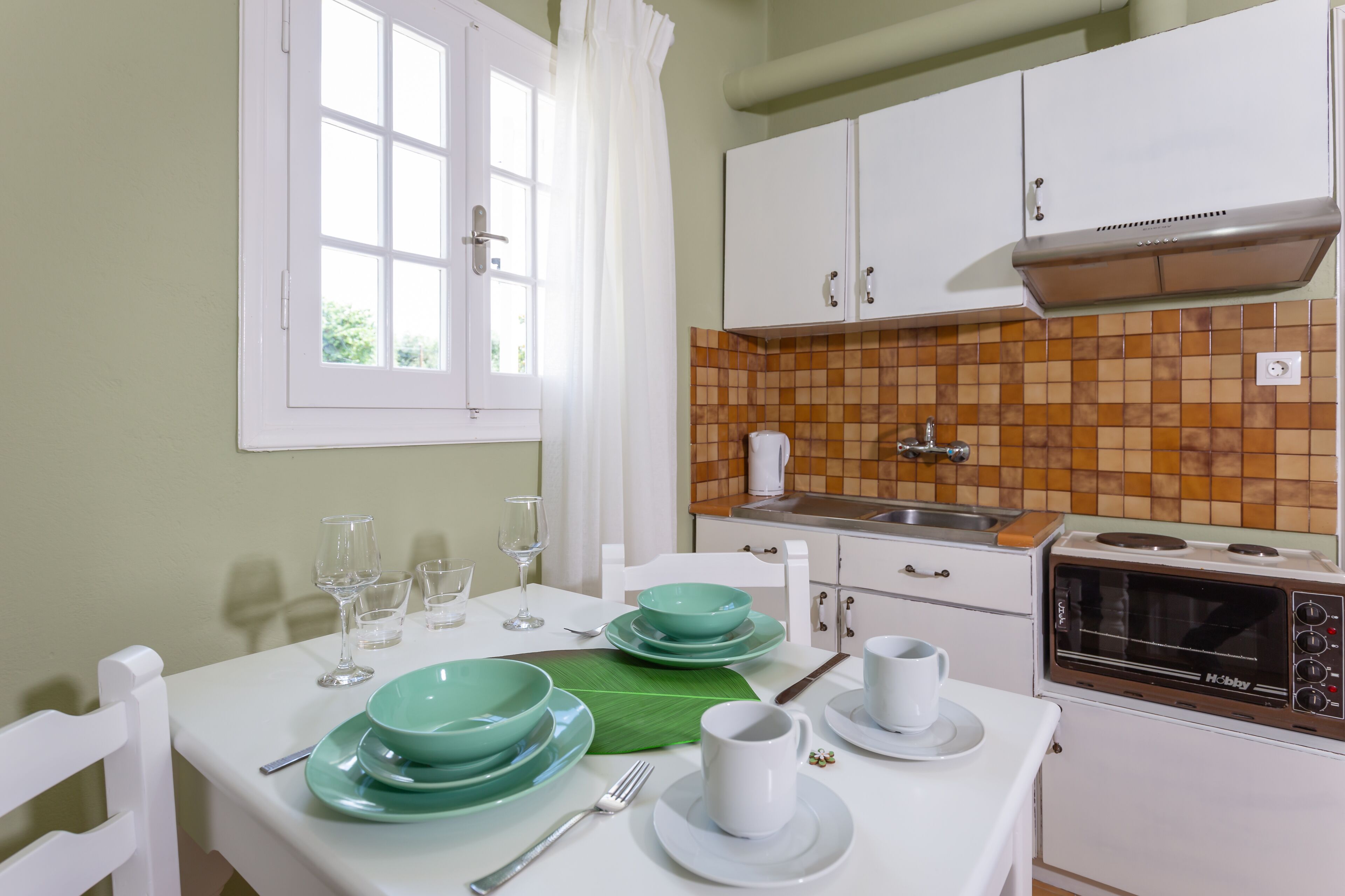 A kitchen with white cabinets, a tiled backsplash, a microwave, and a dining table set with plates, glasses, and cutlery.