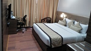 A hotel room with a large bed, a desk with a chair, a television, and curtains. - Hotel Ramaya  (Gwalior)