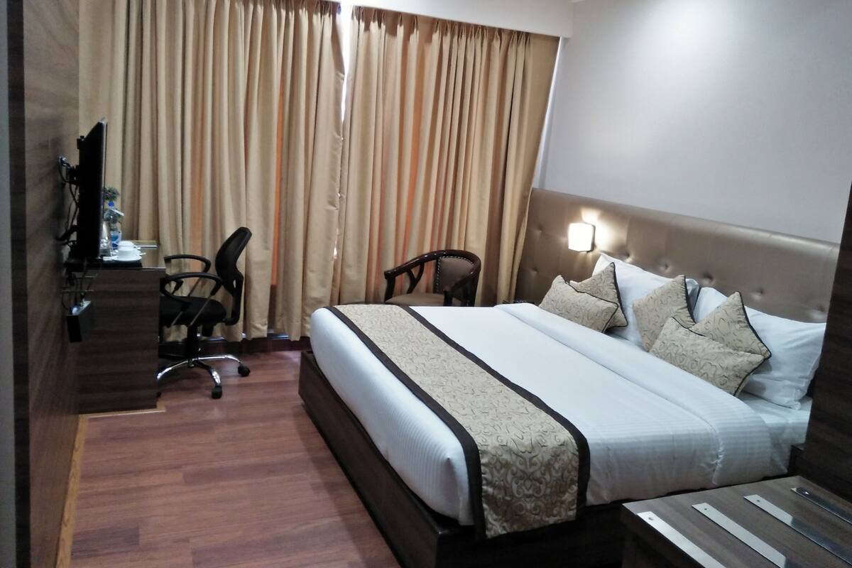 A hotel room with a large bed, a desk with a chair, a television, and curtains.