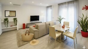 A modern living room with a sofa, dining table, and chairs, a flat-screen TV, and potted plants. - La Terrazza di Andrea (Imperia)