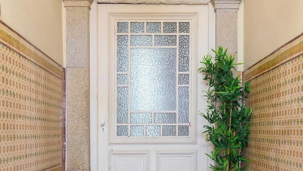 Una puerta blanca con diseños de vidrio intrincados, flanqueada por paredes con motivos decorativos y una planta en maceta.