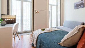 Un dormitorio con una cama, un escritorio con una computadora, una silla y una ventana.
