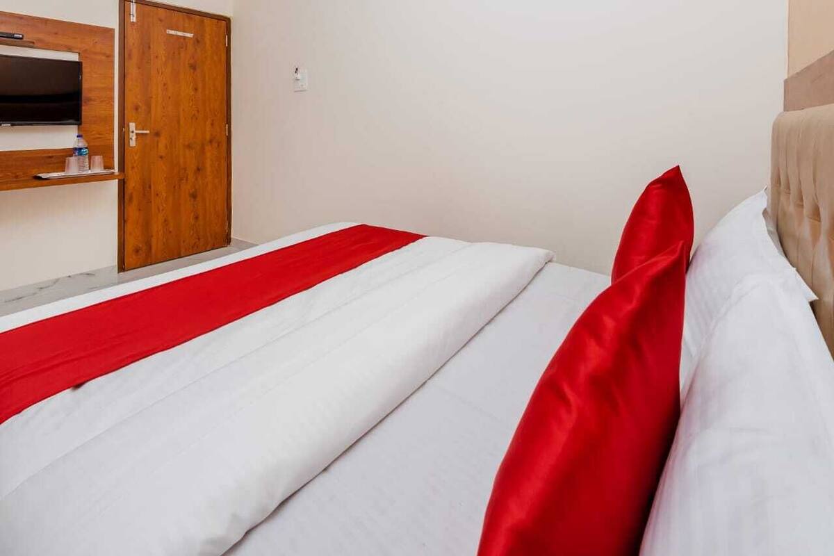 A hotel room with a bed, a wooden wardrobe, and a television on the wall.