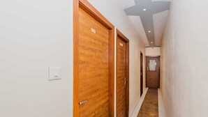 A hallway with wooden doors numbered 103 and 104, a light switch, and a tiled floor. - Hotel Purple Orchid (Mumbai)