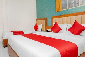 Un lit double avec une literie blanche et rouge, une tête de lit en bois et un téléphone sur la table de chevet.