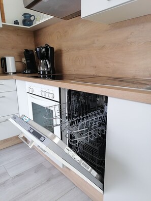 Una cocina moderna con lavavajillas integrado, cafetera y hervidor sobre la encimera.