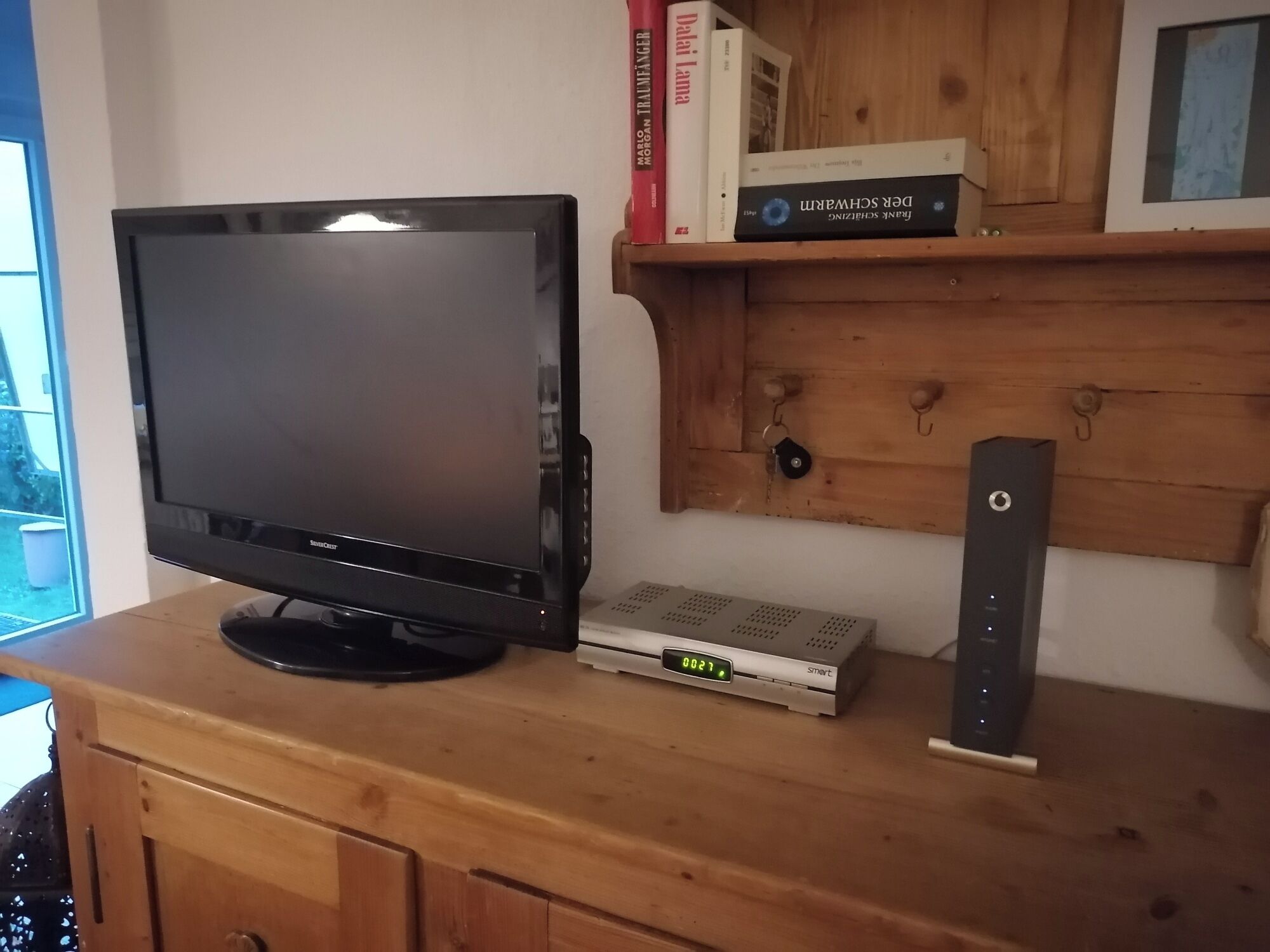 A television on a wooden cabinet, a digital clock displaying 02:27, and a small speaker.