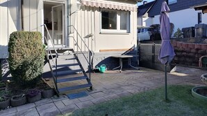 Une maison blanche avec un toit en tuiles, une porte d’entrée et un petit porche avec des marches menant à l’entrée.