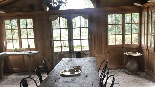Un coin repas rustique en bois, avec une grande table, des chaises et une vue dégagée grâce à de larges fenêtres.